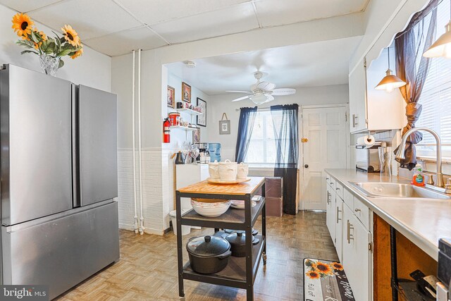 kitchen with ceiling fan, sink, stainless steel fridge, light parquet floors, and white cabinets