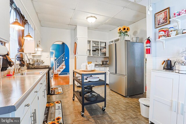 kitchen with white cabinets, stainless steel appliances, a drop ceiling, and hanging light fixtures