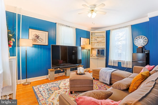 living room featuring built in shelves, ceiling fan, and wood-type flooring