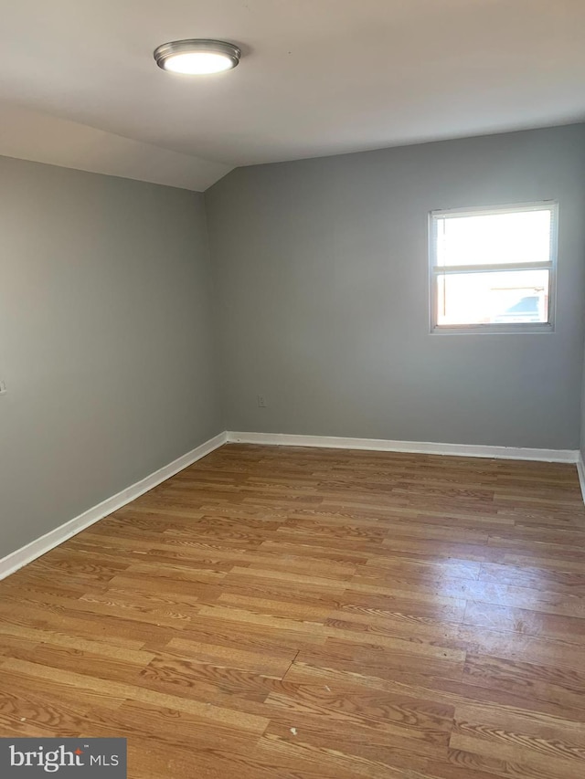 unfurnished room with vaulted ceiling and light wood-type flooring