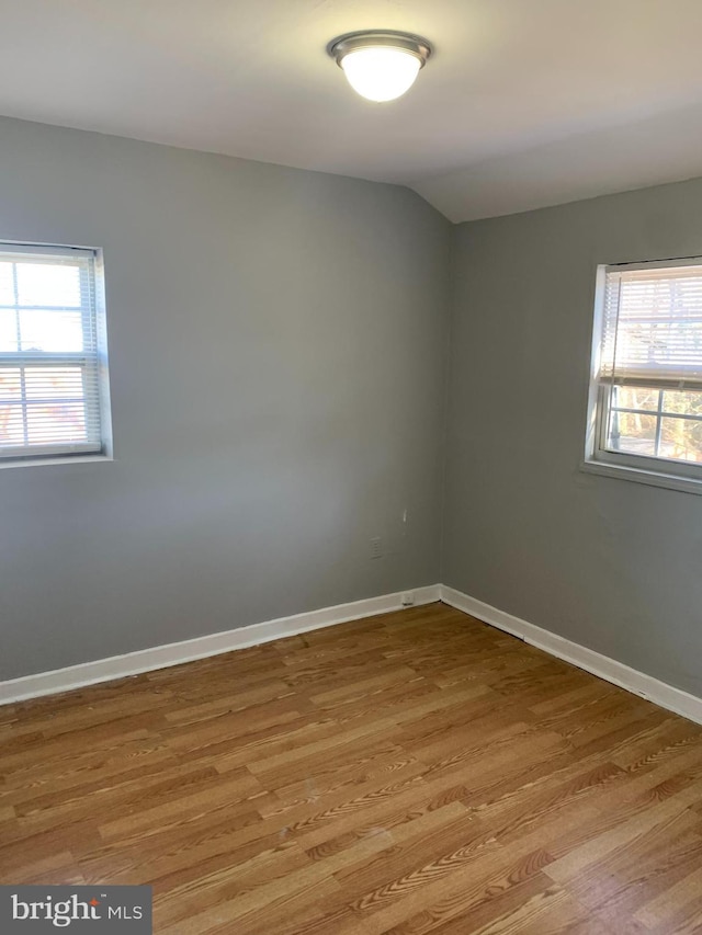 empty room featuring plenty of natural light, light wood-type flooring, and vaulted ceiling