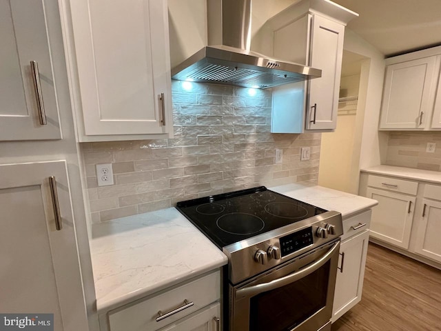 kitchen featuring wall chimney exhaust hood, light hardwood / wood-style flooring, stainless steel range with electric cooktop, decorative backsplash, and white cabinets