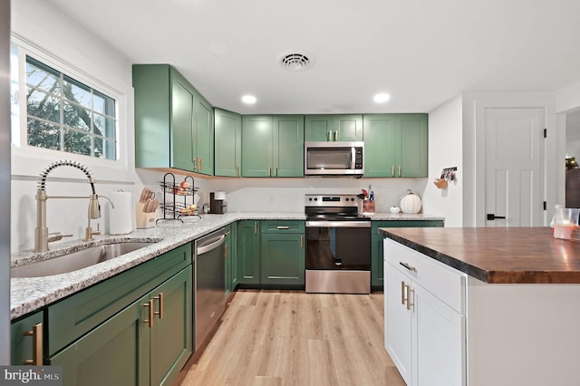 kitchen featuring light stone countertops, stainless steel appliances, sink, light hardwood / wood-style floors, and green cabinets