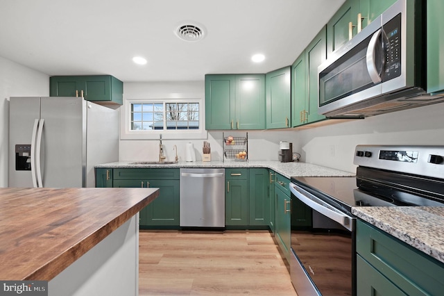 kitchen featuring sink, green cabinetry, light wood-type flooring, butcher block countertops, and stainless steel appliances