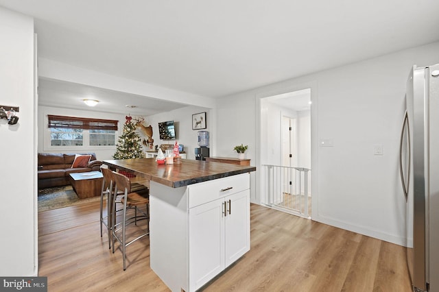 kitchen featuring white cabinetry, stainless steel fridge, a kitchen bar, a kitchen island, and light wood-type flooring