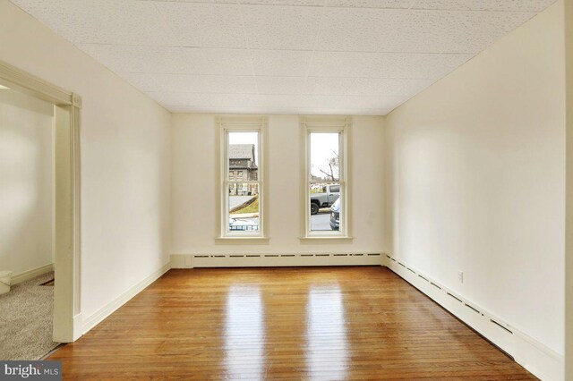 unfurnished room with light wood-type flooring and a baseboard heating unit