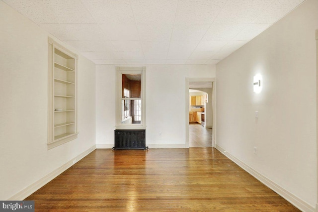 unfurnished living room with built in shelves, wood-type flooring, and radiator