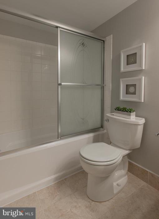 bathroom featuring shower / bath combination with glass door, tile patterned floors, and toilet