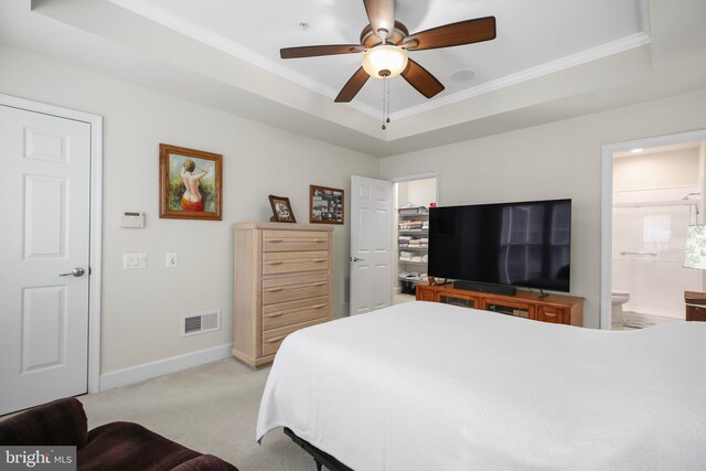 bedroom with a raised ceiling, light colored carpet, ceiling fan, and ensuite bathroom