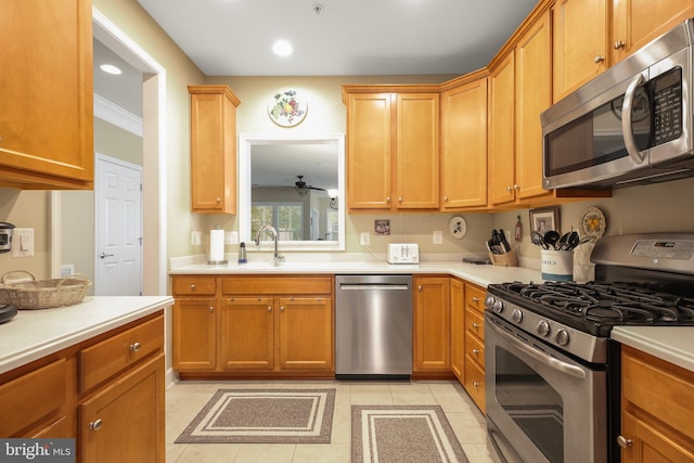 kitchen featuring ceiling fan, sink, appliances with stainless steel finishes, ornamental molding, and light tile patterned floors