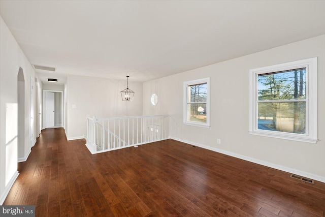 unfurnished room with a chandelier, a wealth of natural light, and dark wood-type flooring