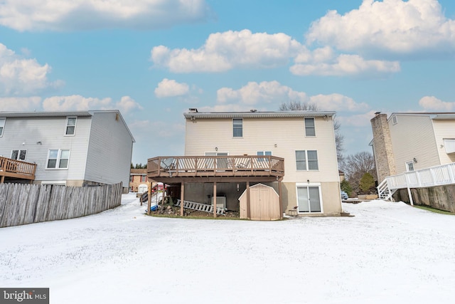 snow covered house featuring a wooden deck and a storage unit