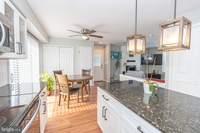 kitchen with decorative light fixtures, white cabinetry, a large fireplace, light wood-type flooring, and ceiling fan