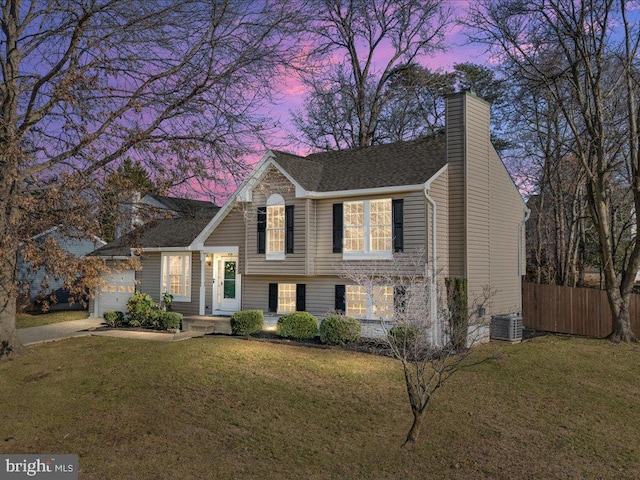 split level home with central air condition unit, a garage, and a lawn