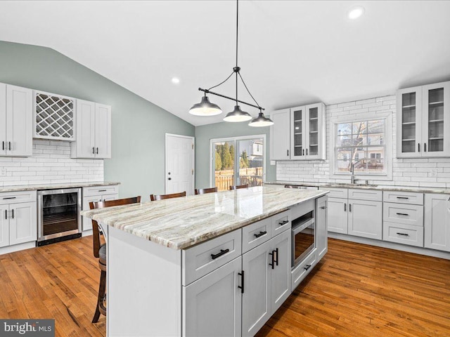 kitchen featuring decorative backsplash, a kitchen breakfast bar, wine cooler, a center island, and white cabinetry