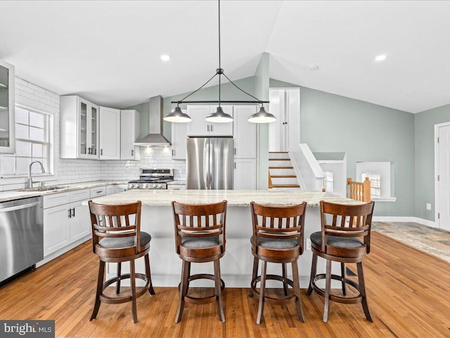 kitchen with sink, wall chimney exhaust hood, appliances with stainless steel finishes, decorative light fixtures, and a kitchen island