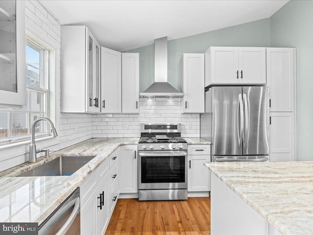 kitchen with sink, vaulted ceiling, wall chimney exhaust hood, white cabinetry, and stainless steel appliances