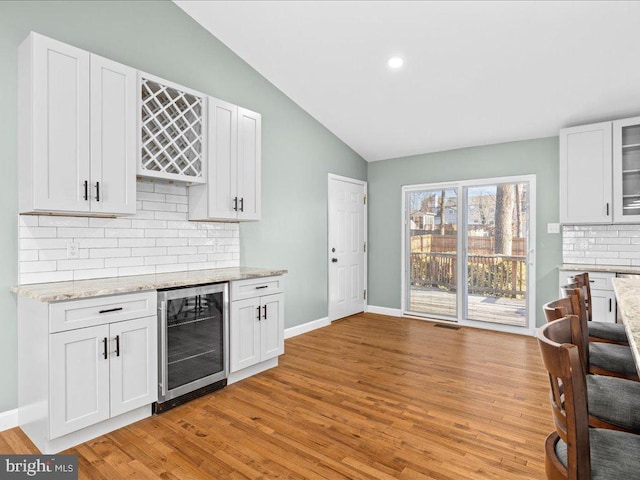 kitchen featuring lofted ceiling, white cabinetry, backsplash, and wine cooler