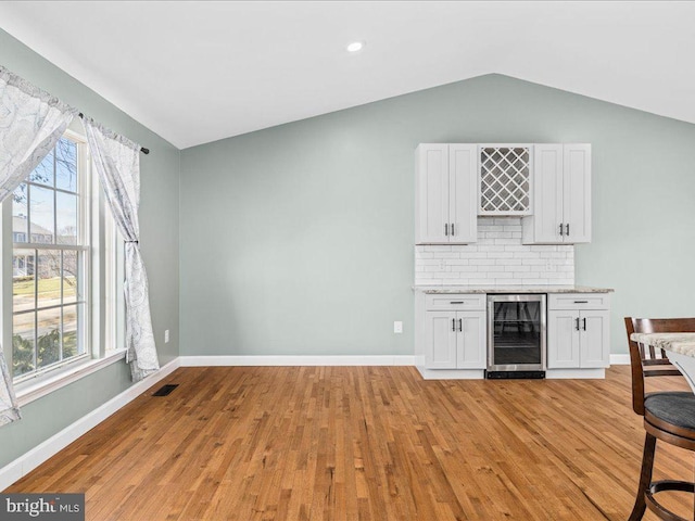 bar with decorative backsplash, light wood-type flooring, vaulted ceiling, beverage cooler, and white cabinets