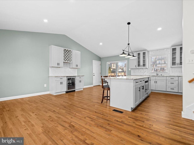 kitchen with lofted ceiling, white cabinets, hanging light fixtures, a breakfast bar area, and beverage cooler