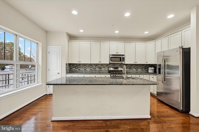 kitchen featuring a kitchen island with sink, appliances with stainless steel finishes, sink, and dark stone counters