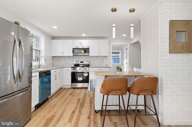 kitchen with white cabinetry, a kitchen bar, stainless steel appliances, pendant lighting, and sink