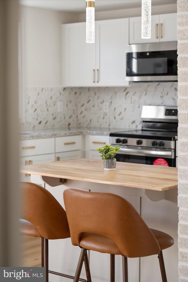 kitchen featuring backsplash, a kitchen breakfast bar, stainless steel appliances, white cabinets, and wood counters