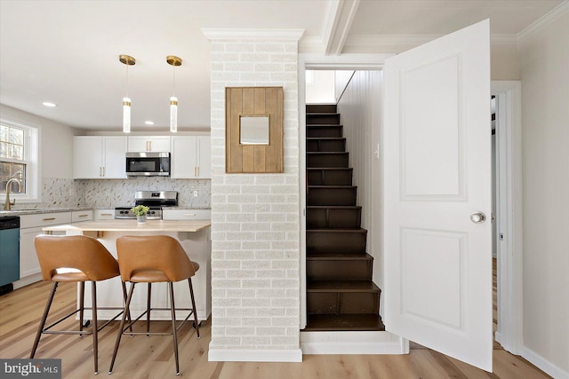 kitchen featuring white cabinetry, a breakfast bar area, appliances with stainless steel finishes, pendant lighting, and sink