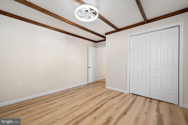 unfurnished bedroom with light hardwood / wood-style floors, a closet, and beam ceiling