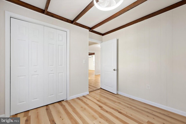 unfurnished bedroom with ceiling fan, a closet, beamed ceiling, and light wood-type flooring