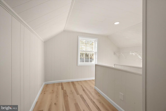 bonus room featuring vaulted ceiling, wooden walls, and light wood-type flooring