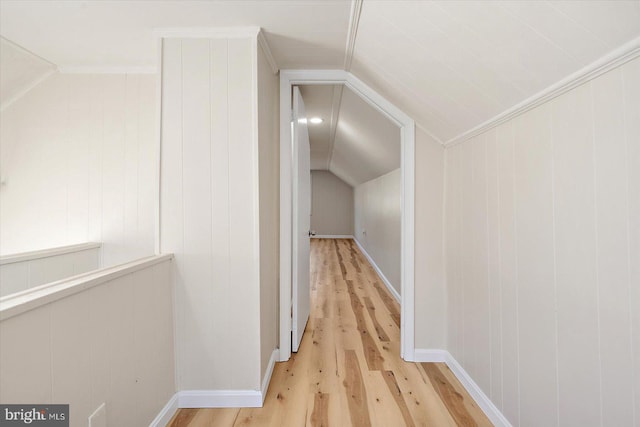 corridor with light wood-type flooring, ornamental molding, and vaulted ceiling