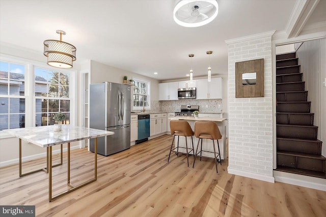 kitchen featuring white cabinetry, stainless steel appliances, decorative backsplash, a kitchen breakfast bar, and hanging light fixtures