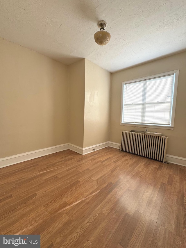 empty room featuring hardwood / wood-style floors, a textured ceiling, and radiator