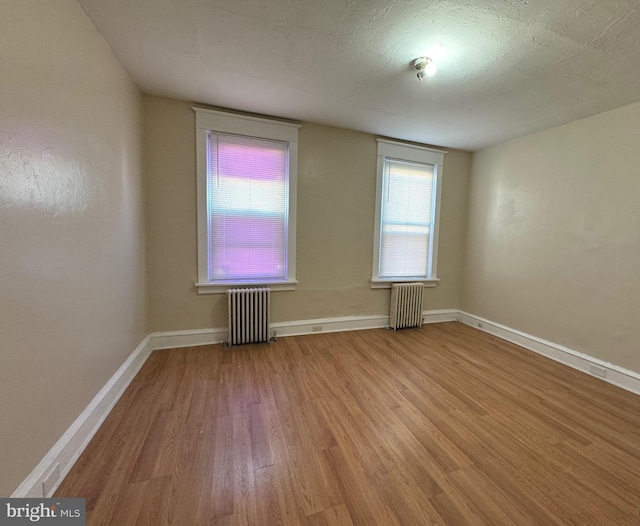 unfurnished room with radiator heating unit, a textured ceiling, and light hardwood / wood-style flooring