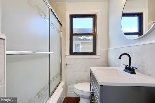 full bathroom featuring toilet, vanity, tile walls, and bath / shower combo with glass door