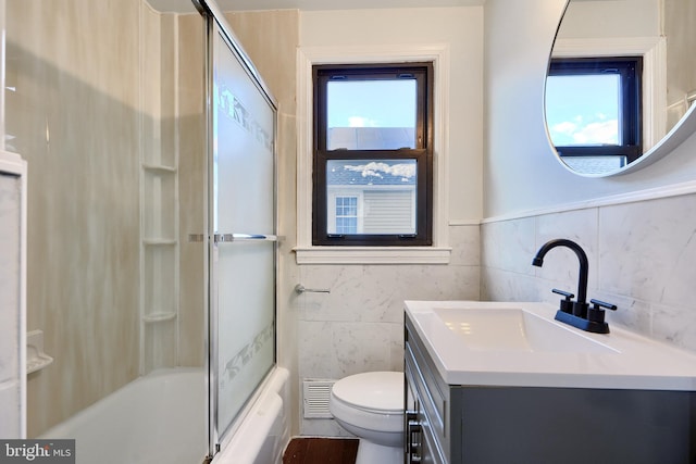 full bathroom with tile walls, toilet, a healthy amount of sunlight, and vanity