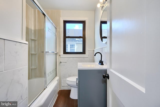 full bathroom with toilet, hardwood / wood-style floors, tile walls, bath / shower combo with glass door, and vanity