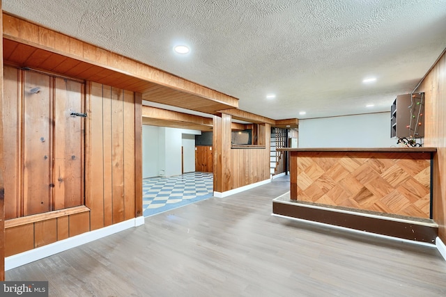 interior space with a textured ceiling, wood walls, kitchen peninsula, and wood-type flooring