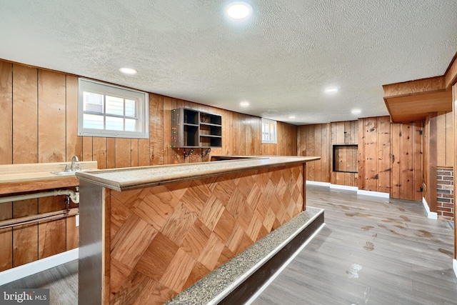 bar with a textured ceiling, light hardwood / wood-style floors, wood walls, and sink