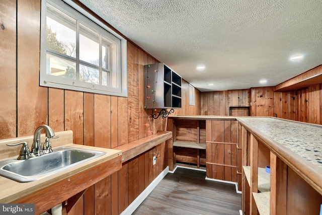 bar with a textured ceiling, wood walls, dark hardwood / wood-style floors, and sink