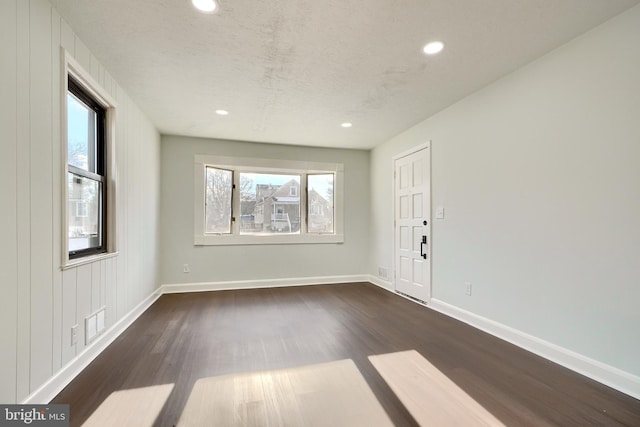 empty room with dark wood-type flooring, a textured ceiling, and plenty of natural light