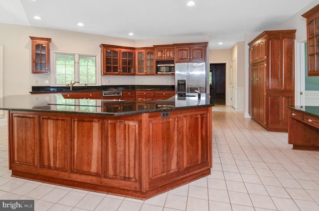 kitchen with light tile patterned floors, stainless steel appliances, glass insert cabinets, and a kitchen island with sink