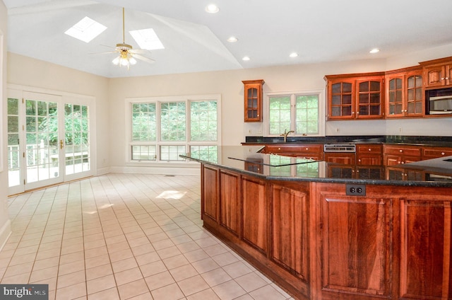 kitchen with light tile patterned floors, vaulted ceiling with skylight, black electric stovetop, ceiling fan, and sink