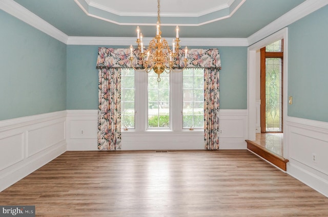 spare room featuring a raised ceiling, a notable chandelier, crown molding, and light hardwood / wood-style floors