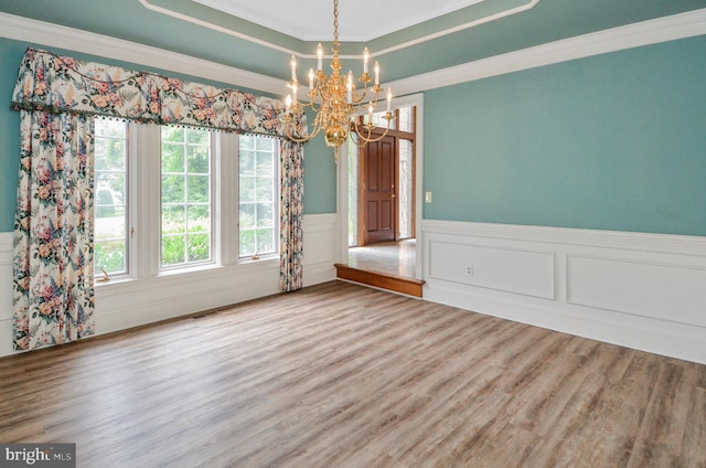 unfurnished dining area featuring visible vents, a raised ceiling, wainscoting, ornamental molding, and wood finished floors