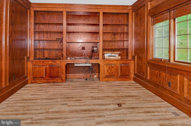 unfurnished office with light wood-type flooring, built in study area, visible vents, and wooden walls