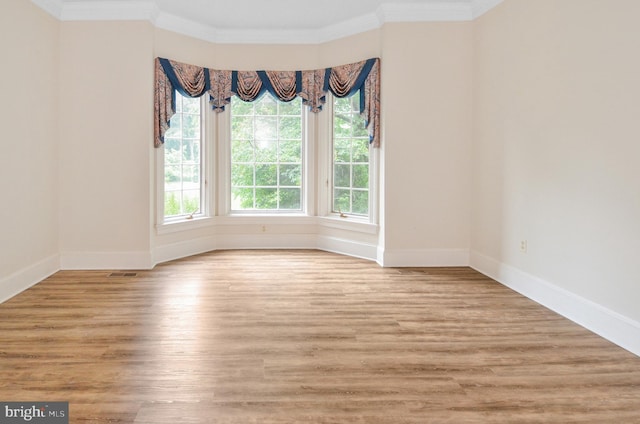 unfurnished room featuring ornamental molding, light wood-type flooring, visible vents, and baseboards