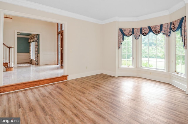 spare room with a decorative wall, stairway, light wood-style floors, and ornamental molding