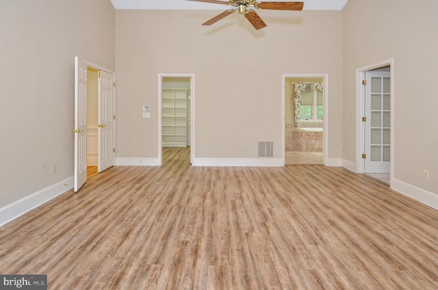 spare room with light wood-style flooring, visible vents, baseboards, ceiling fan, and a high ceiling